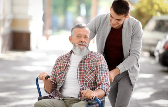 Man helping an elderly man in a wheelchair - The Stress of Being a Caregiver: Finding Support for Your Mental Health - Article by The Therapy Centre