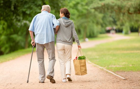 A woman helping an elderly man with groceries and walking - The Stress of Being a Caregiver: Finding Support for Your Mental Health - Article by The Therapy Centre